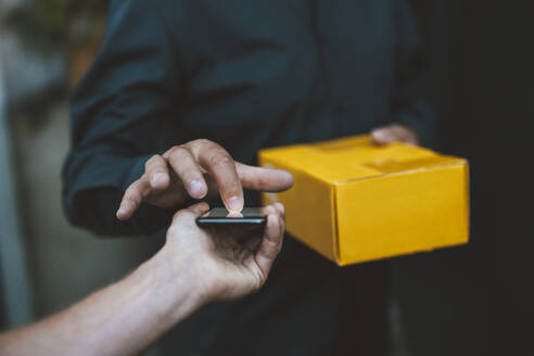 Ein älterer Mann unterschreibt auf einem Mobiltelefon, das von einem Zusteller gehalten wird - GUSF07003