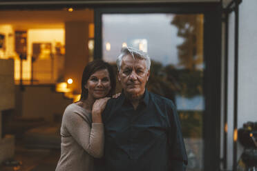Lächelnde Frau mit älterem Mann vor einem Haus in der Abenddämmerung stehend - GUSF07008