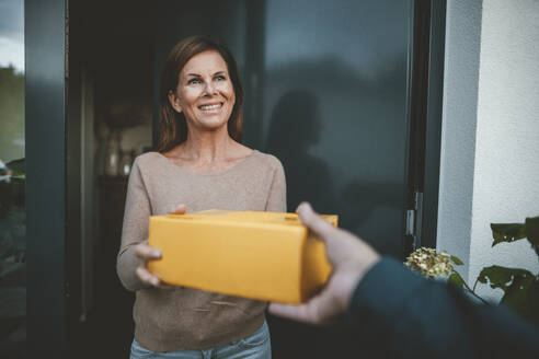 Happy woman receiving package from delivery person at doorway - GUSF07024