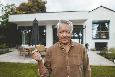 Smiling senior man with white hair holding credit card at backyard - GUSF07031