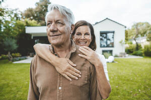 Glückliche Frau umarmt älteren Mann von hinten im Hinterhof - GUSF07061