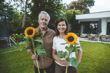 Lächelnder Mann und Frau halten Sonnenblumen im Garten - GUSF07066