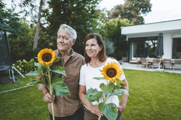 Lächelnder älterer Mann mit Frau, die Sonnenblumen im Hinterhof hält - GUSF07067