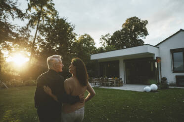 Couple looking at each other standing in garden at sunset - GUSF07072