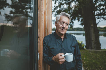 Älterer Mann mit Kaffeetasse an einer Glaswand im Hinterhof stehend - GUSF07079