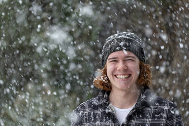 Smiling young man in knit hat enjoying snowfall - LBF03628