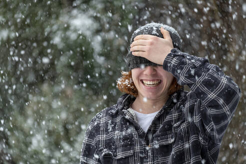 Fröhlicher Mann, der bei Schneefall seine Augen mit einer Strickmütze bedeckt - LBF03629
