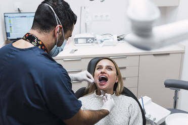 Zahnärztin prüft die Zähne eines Patienten im Behandlungsraum einer Klinik - PNAF03055