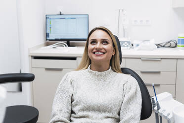 Smiling young woman sitting on dentist chair at clinic - PNAF03067