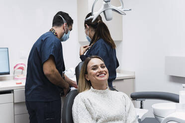 Happy young woman sitting on dentist's chair at clinic - PNAF03070