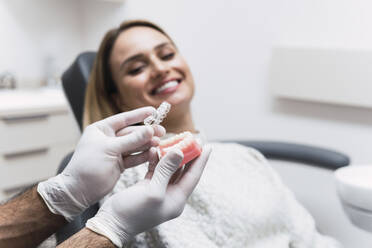 Zahnarzt hält Zahnersatz am Patienten im Behandlungszimmer - PNAF03073