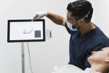 Dentist showing teeth X-ray to patient over intraoral scanner screen in clinic - PNAF03076