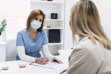 Arzt mit Gesichtsschutzmaske diskutiert mit Patientin über Krankenakte in Klinik - PNAF03086