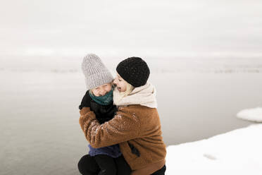 Mutter umarmt Tochter am See im Winter - ANF00082