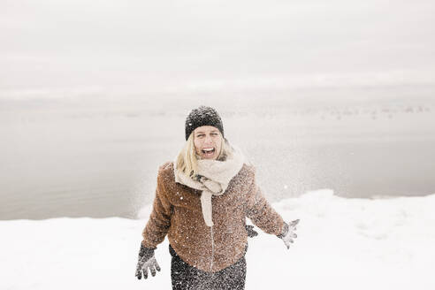 Unbekümmerte Frau in warmer Kleidung, die im Winter mit Schnee spielt - ANF00089