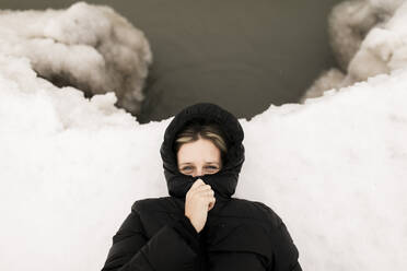 Frau, die ihr Gesicht mit einem Kapuzenpulli bedeckt, liegt im Winter im Schnee - ANF00099