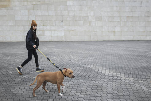 Woman with dog walking on footpath by wall - MTBF01157