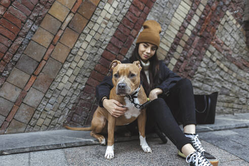 Junge Frau mit Hund vor einer Mauer sitzend - MTBF01161