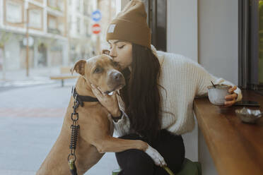 Junge Frau küsst Hund, der in einem Straßencafé sitzt - MTBF01164