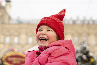 Fröhliches Mädchen mit roter Strickmütze auf dem Weihnachtsmarkt - SSGF00508