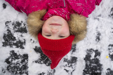 Smiling girl wearing red knit hat lying down on snow - SSGF00511