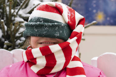 Glückliches Mädchen bedeckt Gesicht mit Strickmütze im Winter - SSGF00513