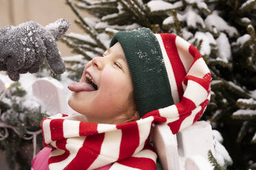 Mädchen mit geschlossenen Augen streckt die Zunge heraus und fängt Schnee im Winter - SSGF00514