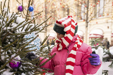 Mädchen in warmer Kleidung berührt den Weihnachtsbaum auf dem Markt - SSGF00515