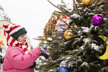 Mädchen mit gestreifter Strickmütze berührt den Weihnachtsbaum - SSGF00516