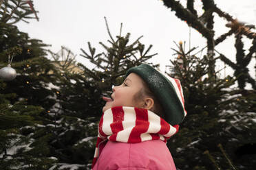 Mädchen streckt die Zunge heraus und steht vor einem Weihnachtsbaum - SSGF00518