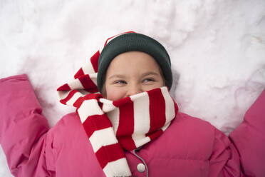 Smiling girl with striped scarf lying down on snow - SSGF00520