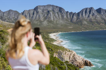Junge Frau fotografiert Berge mit ihrem Smartphone an einem sonnigen Tag - MEF00117