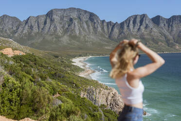 Frau mit Hand in den Haaren betrachtet die Aussicht an einem sonnigen Tag - MEF00119