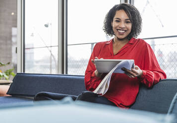 Lächelnde Geschäftsfrau mit Tablet-PC und Dokument am Arbeitsplatz - UUF25410