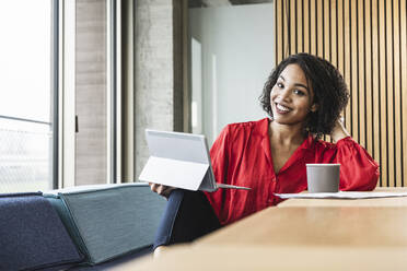 Smiling businesswoman with tablet computer and coffee at desk in office - UUF25412