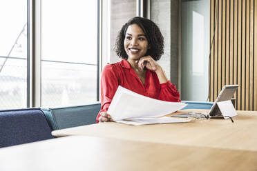 Smiling businesswoman with documents at work place - UUF25415