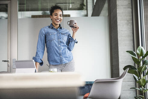 Lächelnde Geschäftsfrau mit Kaffeetasse im Büro - UUF25432
