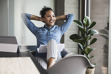 Smiling businesswoman with hands behind head at work place - UUF25442