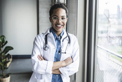 Smiling doctor with arms crossed in clinic - UUF25449