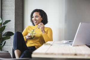 Happy businesswoman with salad bowl at work place - UUF25472