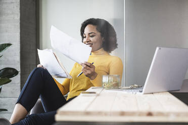 Smiling businesswoman analyzing documents in office - UUF25474