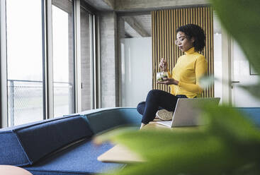 Businesswoman having salad by laptop at desk in office - UUF25489