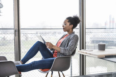 Young businesswoman using tablet PC sitting on chair in office - UUF25497