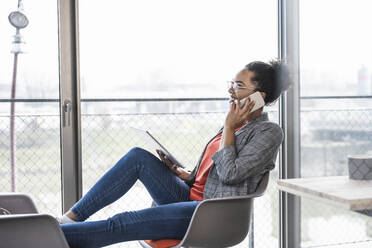 Lächelnde Geschäftsfrau mit Tablet-PC im Gespräch über Smartphone im Büro - UUF25499