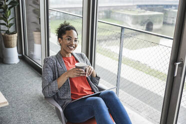 Smiling businesswoman with coffee cup at work place - UUF25502