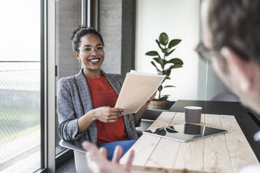 Smiling businesswoman holding documents discussing with colleague in office - UUF25505