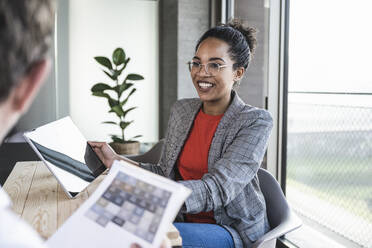 Smiling businesswoman discussing over tablet PC with colleague in office - UUF25509