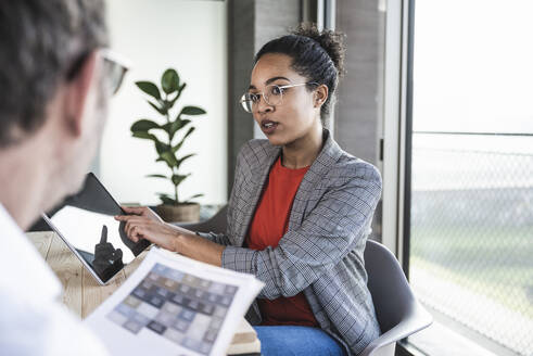 Businesswoman discussing over tablet computer with colleague at work place - UUF25510