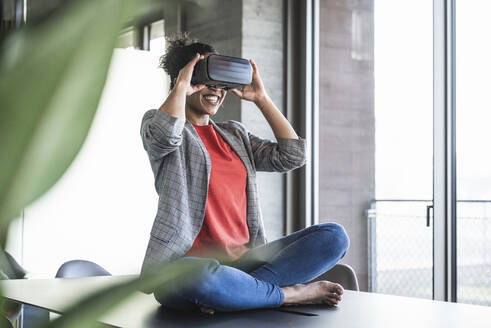 Glückliche Geschäftsfrau, die im Büro durch eine VR-Brille schaut - UUF25522