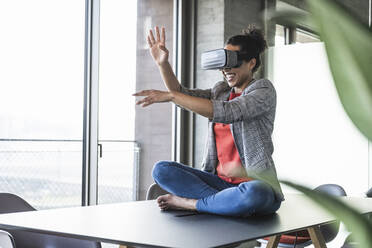 Lächelnde Geschäftsfrau mit VR-Brille gestikuliert im Büro - UUF25524